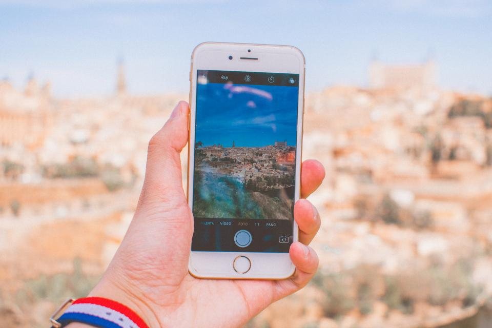 Mão segurando um smartphone diante de uma cidade